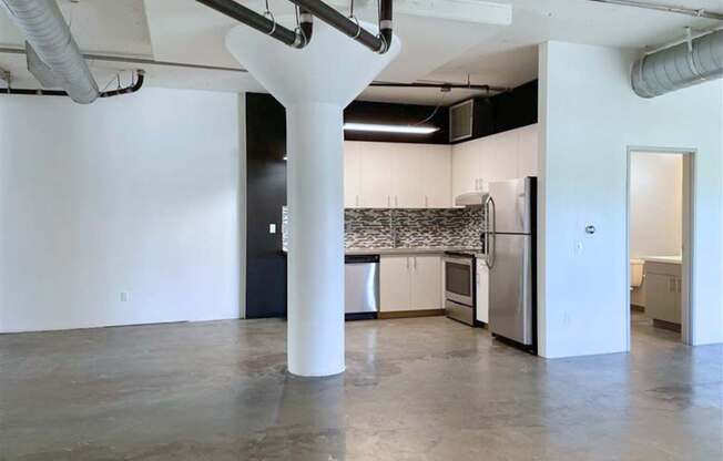 A large white column in the middle of a room with a kitchen in the background.