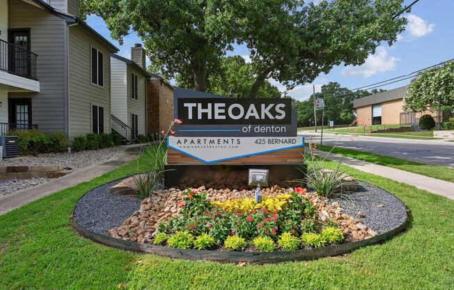 A sign for The Oaks of Denton Apartments is in front of a landscaped area in Denton, TX