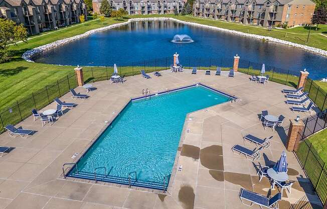 A large swimming pool surrounded by lounge chairs and a pond with a fountain behind it at Oak Shores Apartments, Wisconsin