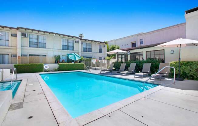 a swimming pool with lounge chairs and umbrellas in front of a building