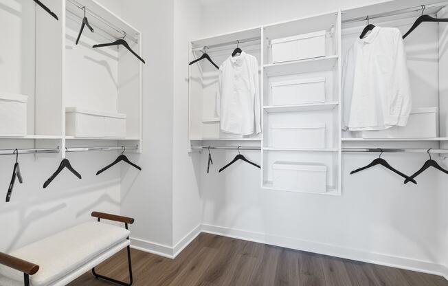 a white closet with white hangers and white shelves and a bench