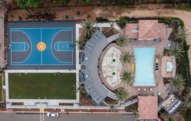 An aerial view of a basketball court and a swimming pool surrounded by palm trees.