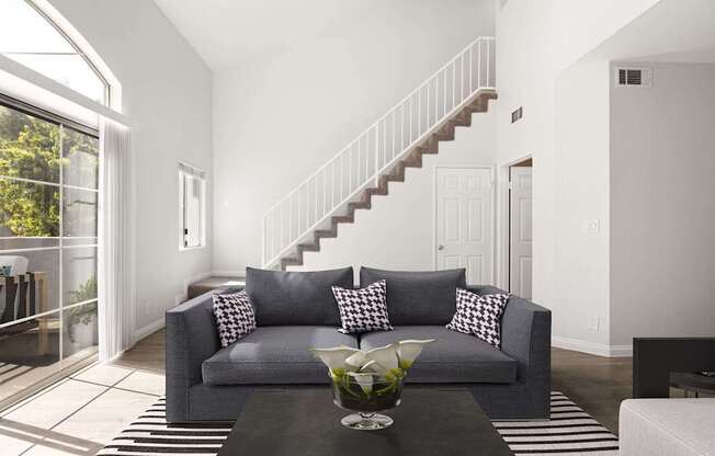 A grey couch with pillows is in the middle of a room with a staircase.