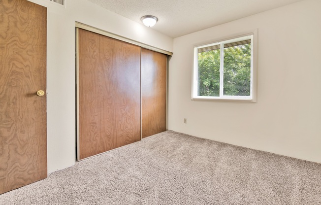 A room with a carpeted floor, a window, and a wooden door.