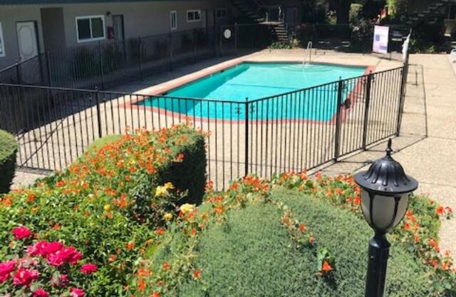 Colonial House Apartments San Jose a pool with a fence and flowers in front of a building