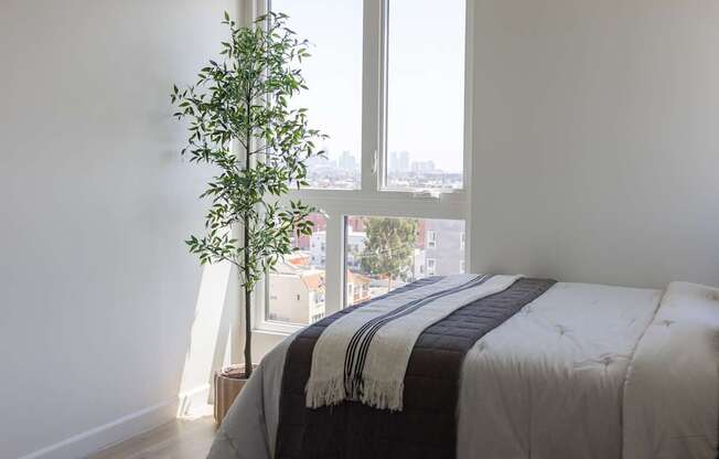 A bedroom with a bed and a plant by the window at Skylar At Sunset Apartments, Los Angeles, California