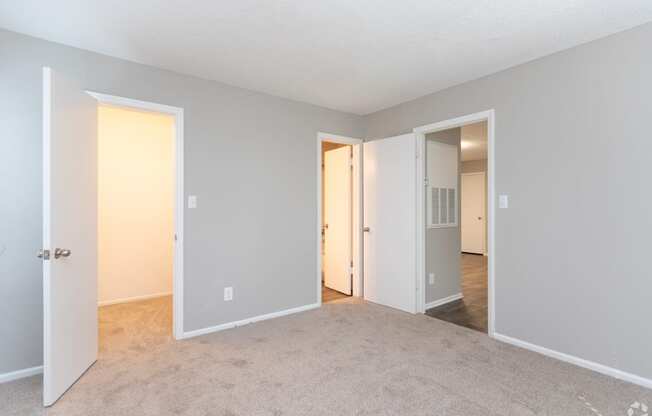 an empty living room with open doors to a hallway and a bedroom