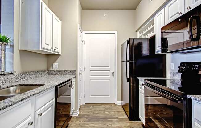 kitchen in one bedroom floorplan with black appliances and wood flooring and granite countertops