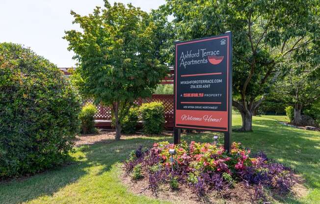 a sign in a park with flowers and trees