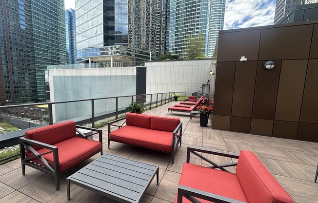 a terrace with red couches and tables on a balcony with skyscrapers
