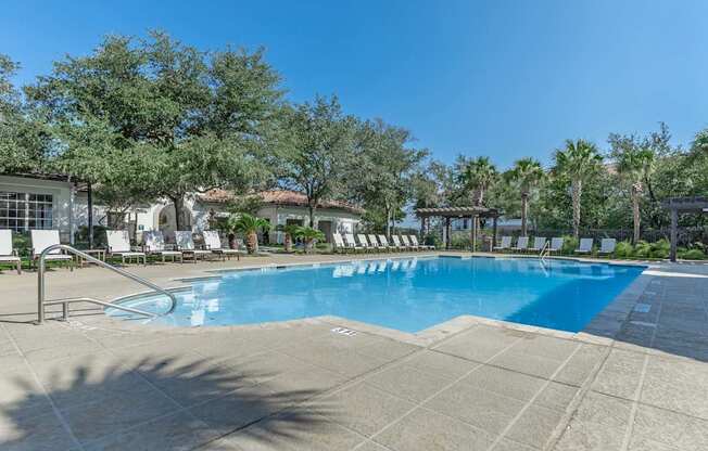 A large swimming pool surrounded by trees and lounge chairs.