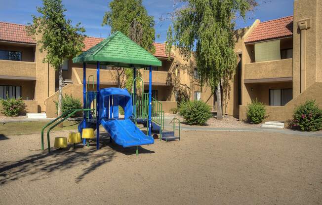 a playground with a blue swing set and a green umbrella