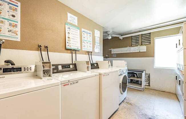 A laundromat with washers and dryers and signs on the wall.