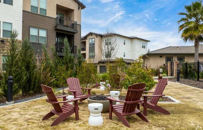 two red adirondack chairs sitting around a fire pit in front of apartments