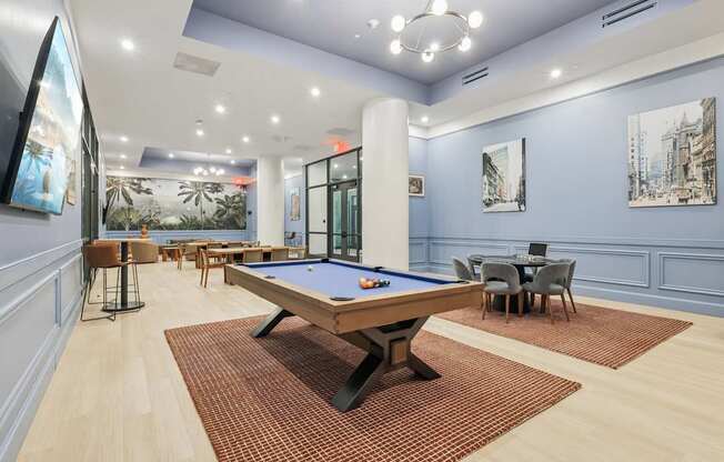 A pool table is in the middle of a room with a blue wall and a painting of a cityscape.