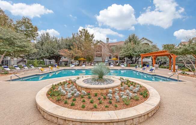 A pool surrounded by a circular flower bed with a palm tree in the middle.