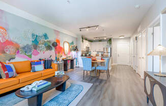 a living room with a couch a table and chairs and a kitchen in the background