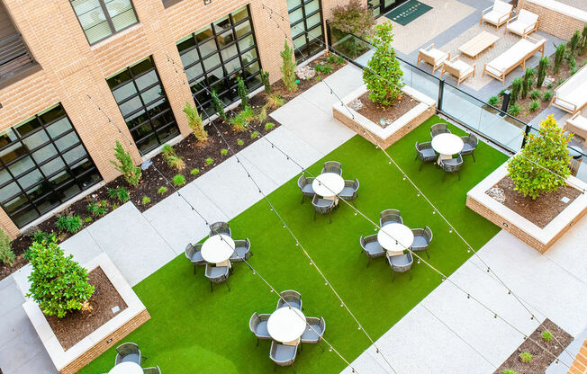 A courtyard with a green lawn and white tables.