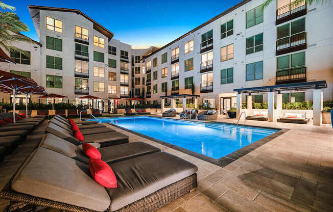 Sparkling pool lit at night, framed by red umbrellas and cushioned loungers for a true resort-style escape