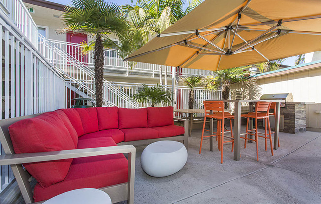 Outdoor resident lounge with a red patio sofa, high table with orange chairs next to the pool, with a gas BBQ at Pacific Sands, San Diego, California