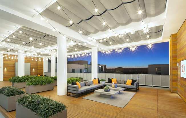 Woodland Hills, CA Apartments - The Q Variel - Penthouse Rooftop with Sofas, Plant Beds, String Lights, Wood-Style Floors and Walls, a TV, and City Views