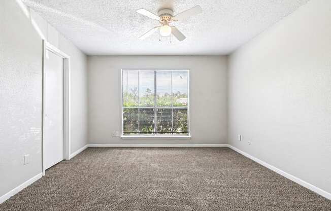 A room with a ceiling fan and a window overlooking a balcony.
