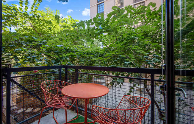 A table and two chairs are on a balcony with a black railing.