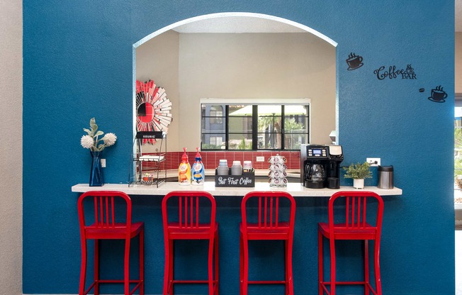a bar with four red stools in front of a counter with red chairs