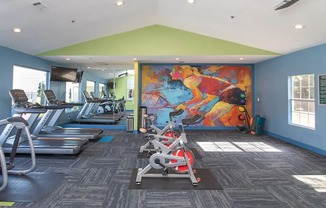 a gym with cardio machines and a colorful mural on the wall