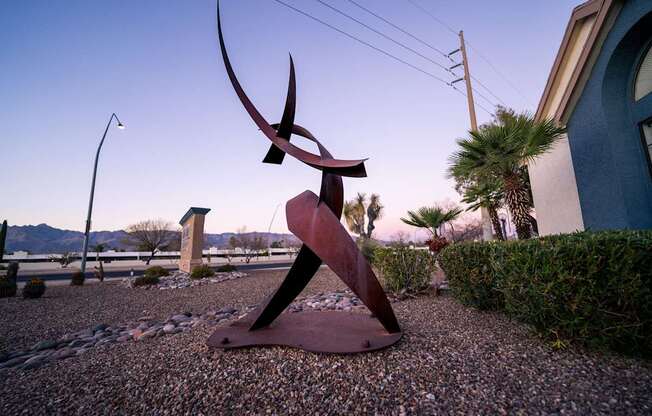 A large metal sculpture of a woman is in the foreground of a gravel area.