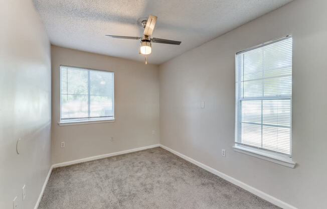 an empty living room with a ceiling fan and two windows