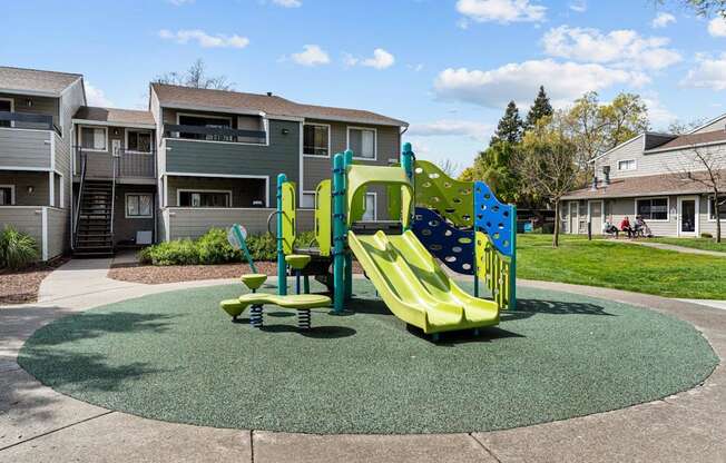 A playground with a green and yellow slide in the middle of a grassy area.