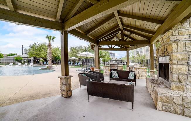 a covered patio with a fireplace and seating next to a pool