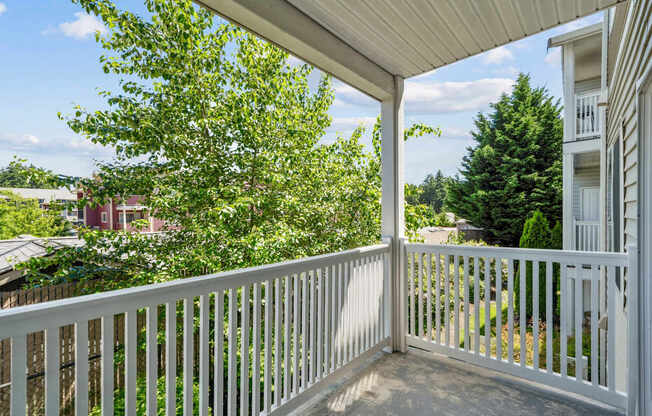 A balcony with white railing overlooking lush trees at The Madison Apartments in Olympia, WA