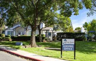 View of the front leasing office with sign that has logo, office and gated pool in the background.