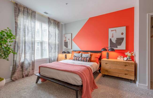 a bedroom with an orange accent wall and a bed with a wooden dresser and bedside