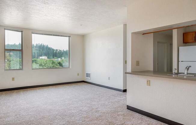 an empty living room with a kitchen and a large window