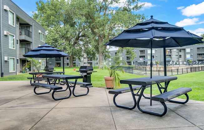 A black and white picnic table with a blue umbrella is in the foreground of a courtyard with apartment buildings in the background.