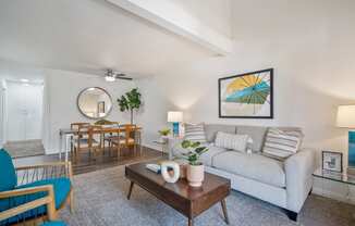 a living room with a couch coffee table and chairs and a dining room table in the background