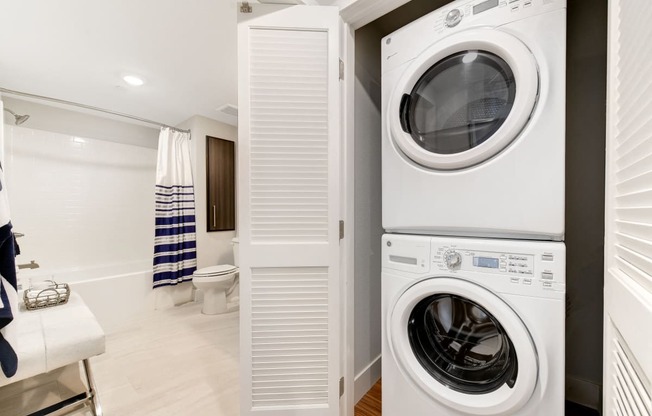 a white washer and dryer in a bathroom with a toilet and a shower