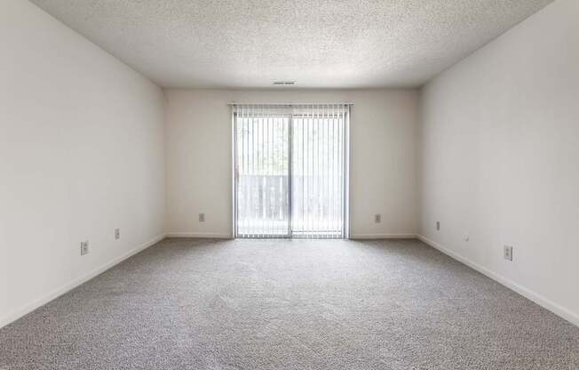 A sparsely furnished room with a carpeted floor and a sliding glass door.