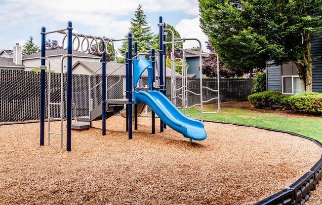 A playground with a blue slide and brown ground cover. at Vibe, Kent, WA