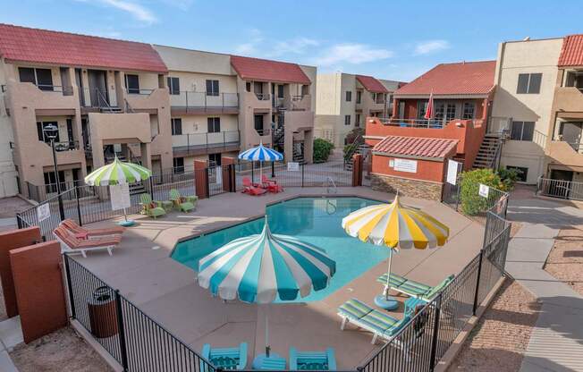 A pool surrounded by a fence and umbrellas in front of apartment buildings. at Urban WalkApartments on 6th Avenue, Phoenix, Arizona
