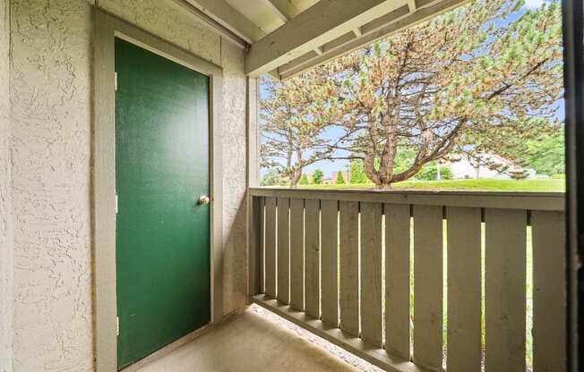 A green door is on the left of a balcony with a view of trees.