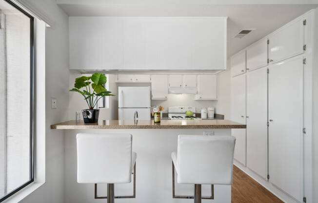 a kitchen with white cabinets and a counter with two white chairs