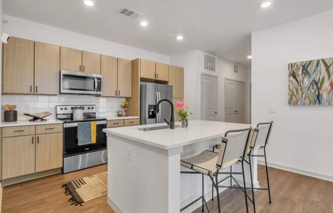 a kitchen with a large island with a white counter top and three chairs