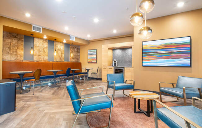a lounge area with blue chairs and a kitchen in the background