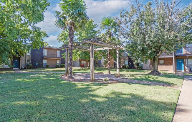 A gazebo and trees in a clearing with apartment buildings in the background at The Drake in Bossier City, LA