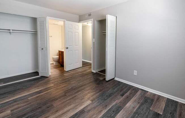 A room with a wooden floor and white walls with a door open to a small room.