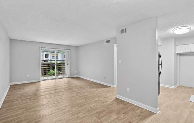 A room with wooden flooring and white walls, with a balcony visible through the door.